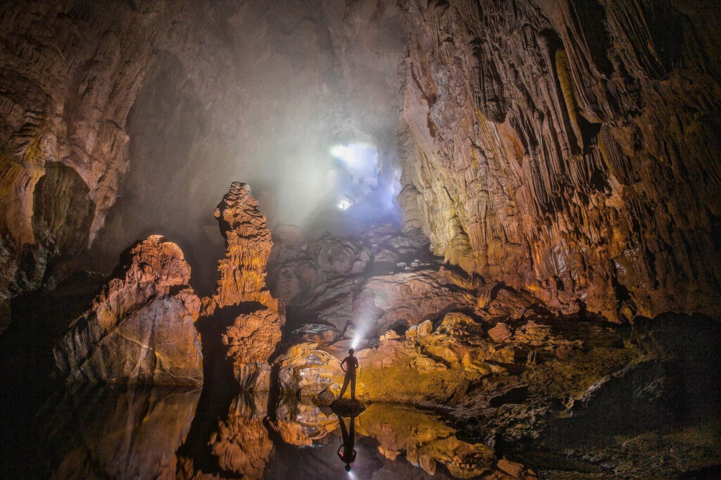 Explorer in Illuminated Cave: Mystical Rock Formations Reflection Wallpaper