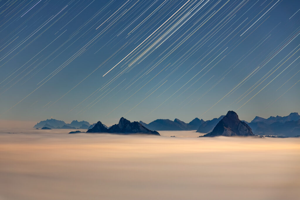 Night landscape with rugged rock formations above fog and blue white star trails wallpaper background