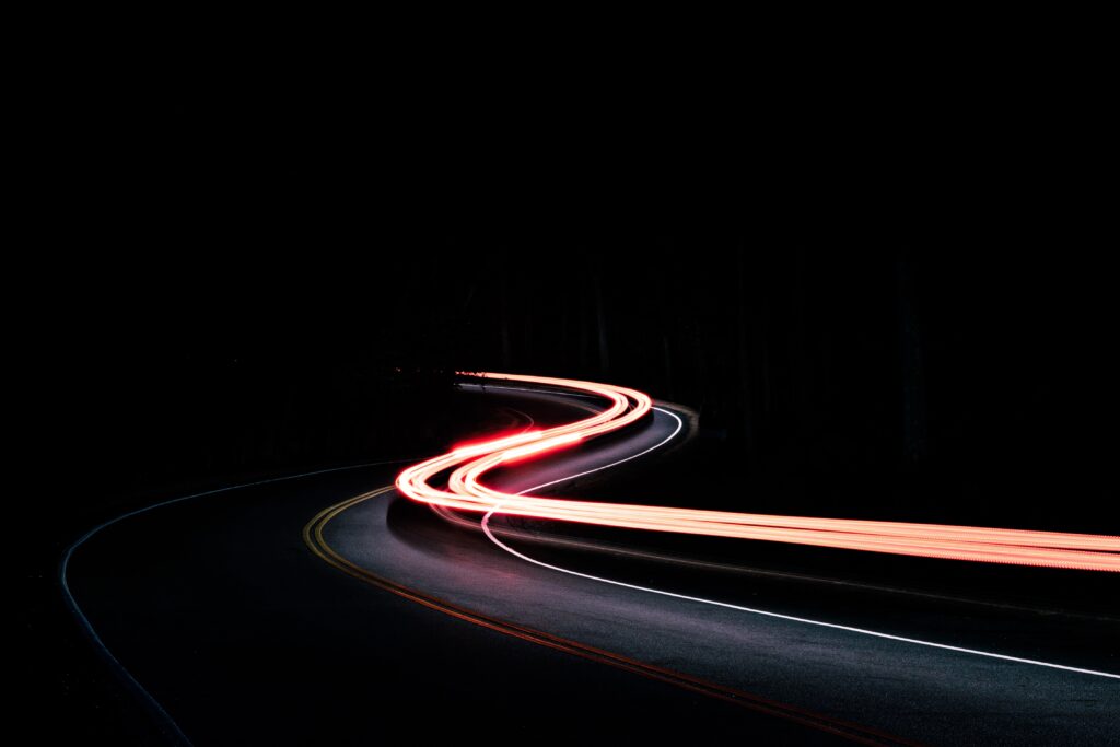 Winding road at night with vibrant red and white car light trails creating dynamic motion Wallpaper