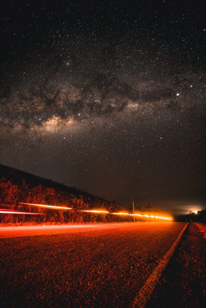 Night road with glowing red light trails under a vast starry sky scenic wallpaper background