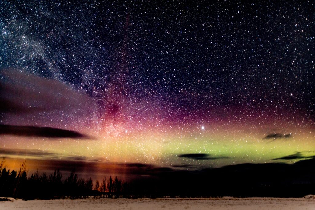 Breathtaking night sky with vibrant aurora and glittering stars over dark silhouetted landscape Wallpaper