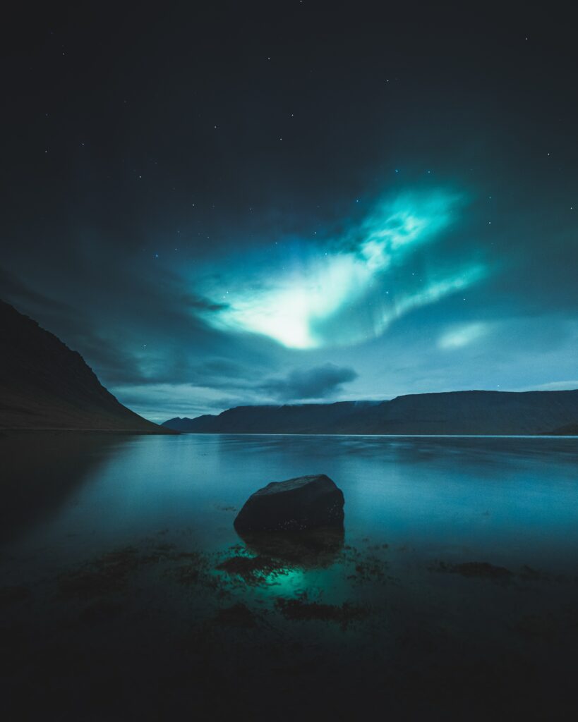 Northern lights over calm lake with silhouetted mountains under starry night sky wallpaper