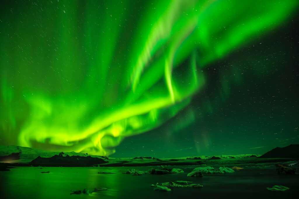 Vivid green northern lights dancing over icy landscape under starry night sky wallpaper background