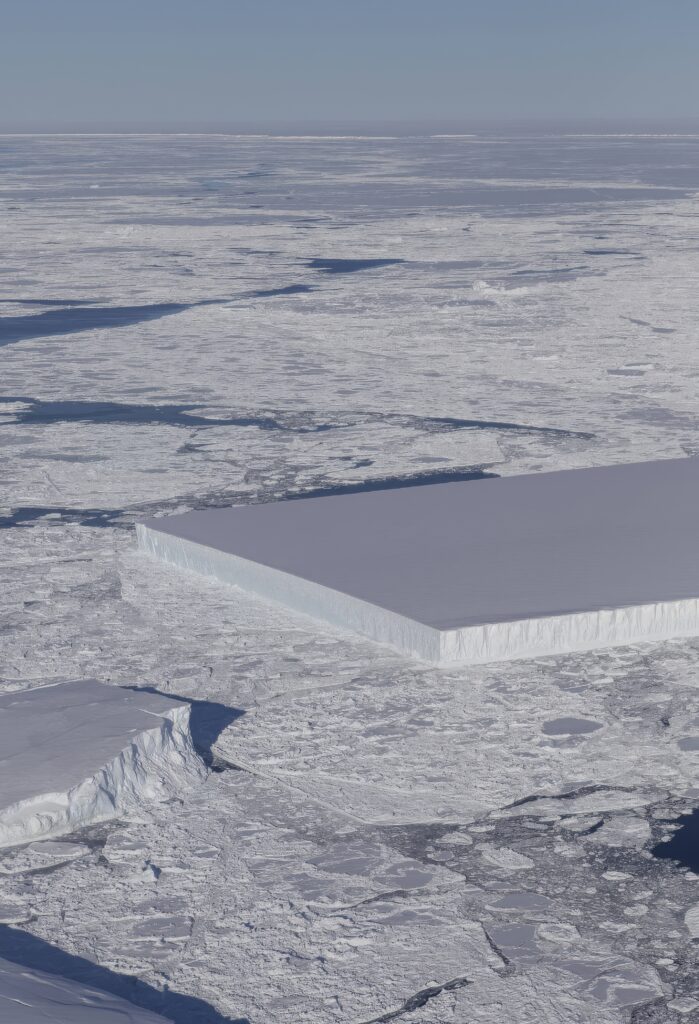 Massive rectangular iceberg floats on icy sea with snow sheets under a crisp blue sky wallpaper