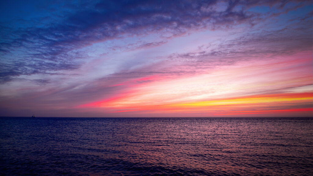 Seascape sunrise with vibrant purple pink yellow clouds over calm rippling ocean peaceful wallpaper
