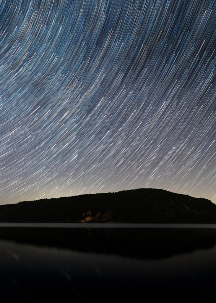 Starry sky with luminous falling star streaks over dark silhouette landscape at night wallpaper