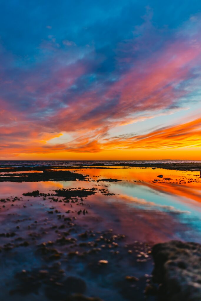 Vibrant sunset horizon with warm oranges cool blues reflecting on calm water serene wallpaper background