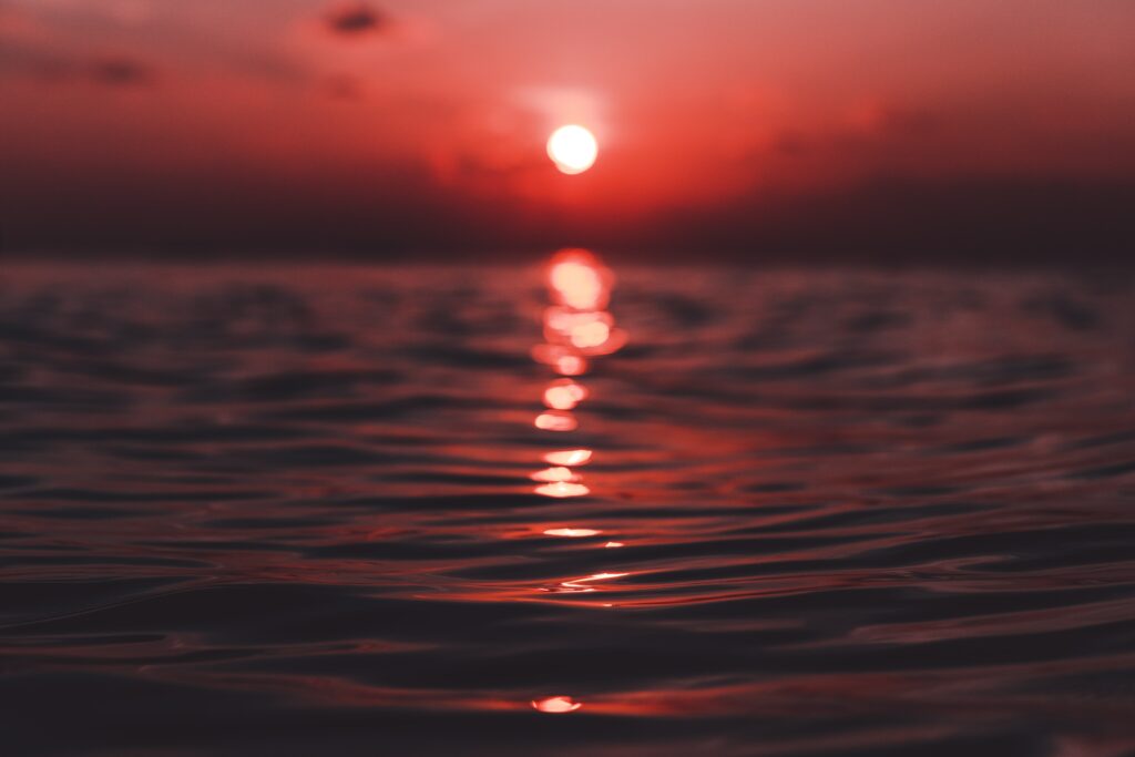 Vivid sunset wallpaper with warm red orange tones reflecting on gentle rippled ocean waves