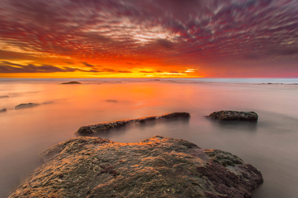 Sunset wallpaper with smooth stones in calm water vibrant orange purple sky reflections background