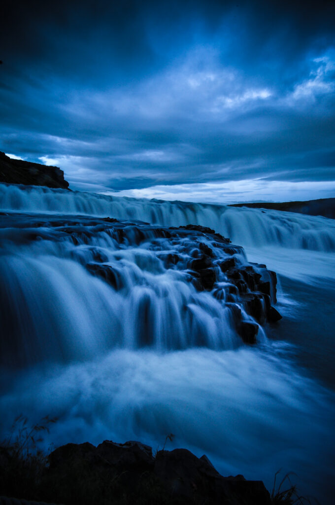 Silky waterfall cascading over dark stones under moody blue sky nature wallpaper background