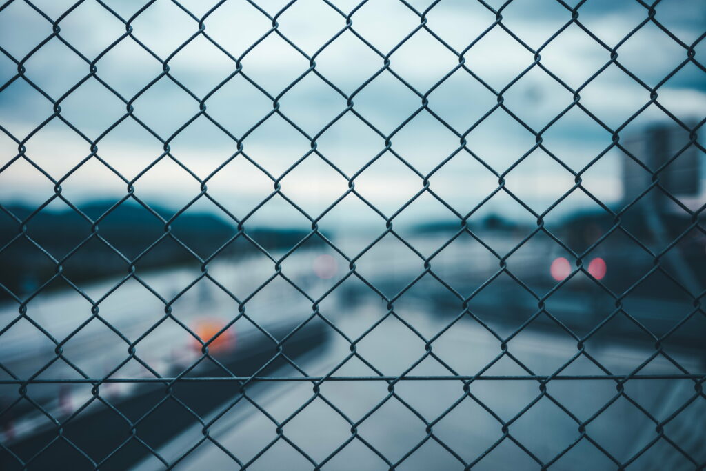 Metal mesh fence with detailed chain links and blurred twilight highway bokeh background wallpaper