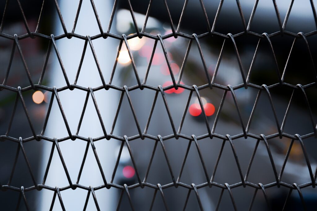 Close-Up Metal Mesh Fence with Blurred Traffic Bokeh Lights Wallpaper