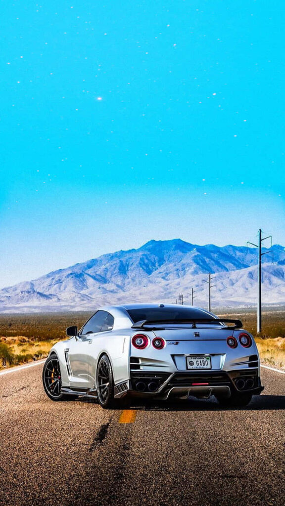 Metallic gray Nissan R35 GTR parked on open road with mountains and bright blue sky background Wallpaper