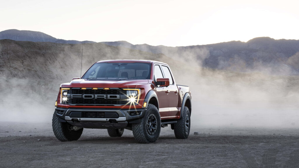 Metallic red Ford F150 Raptor on dusty terrain with rugged mountains misty background wallpaper