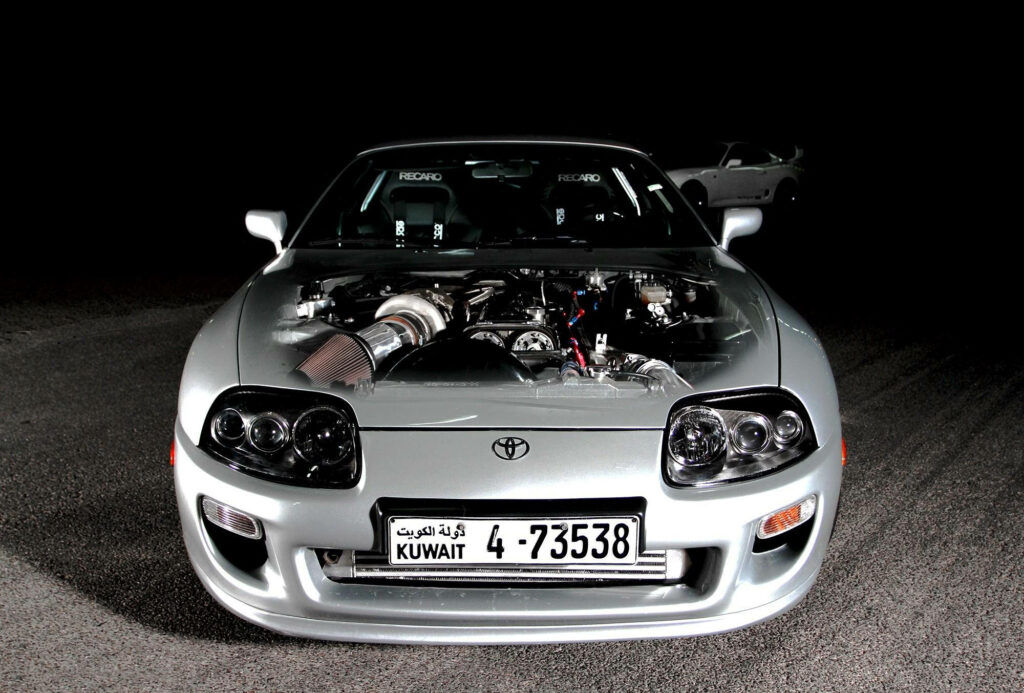 Metallic silver 1994 Toyota Supra Mk4 under spotlight showcasing sleek iconic design and engine Wallpaper