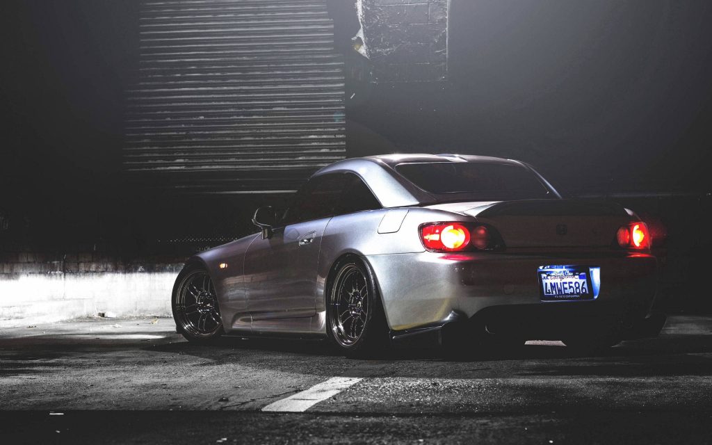 Metallic silver Honda S2000 with slammed stance and custom wheels in moody urban garage Wallpaper