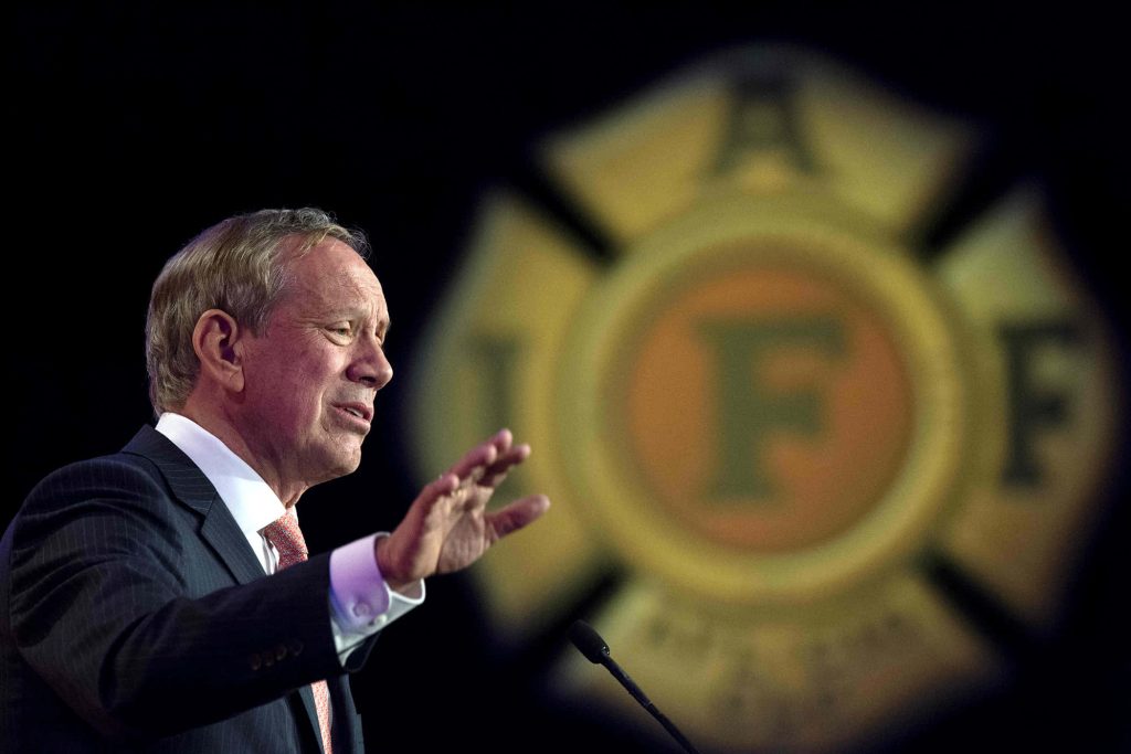Michael Bloomberg speaking at IAFF event podium dramatic lighting political portrait wallpaper
