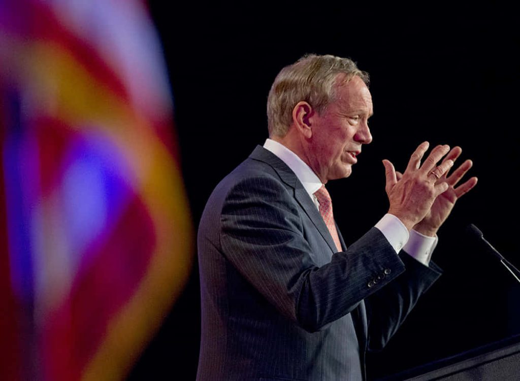 Michael Bloomberg speaking at podium in profile with American flag blurred background lighting Wallpaper
