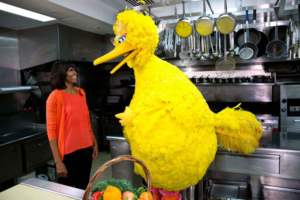 Michelle Obama smiling with Big Bird in a bright kitchen cheerful Sesame Street wallpaper background