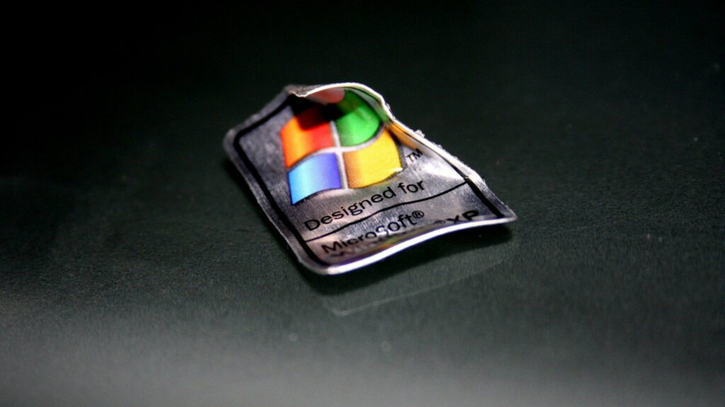 Crumpled metallic Windows XP sticker on dark background, reminiscent of iconic early 2000s OS. Wallpaper