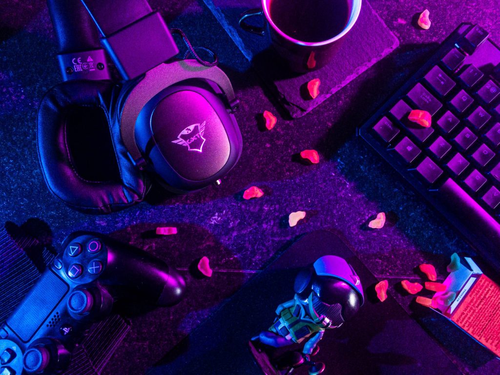 Neon-lit gaming desk flatlay with Trust GXT headset PS4 controller mechanical keyboard and gummies Wallpaper