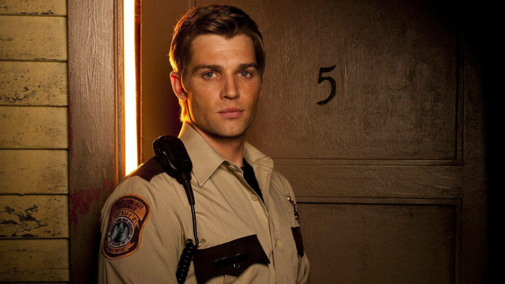 Mike Vogel as law enforcement in Bates Motel uniform standing by dimly lit motel door background Wallpaper