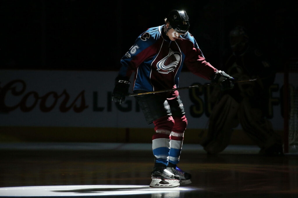 Mikko Rantanen in Colorado Avalanche uniform gripping hockey stick under dramatic spotlight on ice Wallpaper