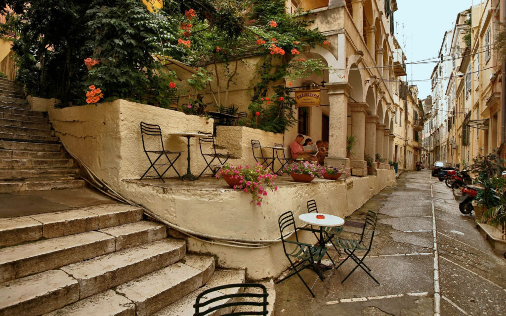 Mikro Cafe Corfu cozy outdoor seating with stone steps vibrant flowers and Mediterranean charm Wallpaper