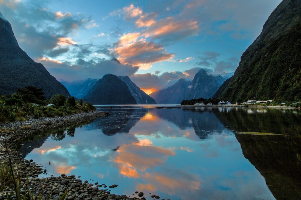 Milford Sound New Zealand sunset with reflective calm bay waters and dramatic mountain landscape Wallpaper