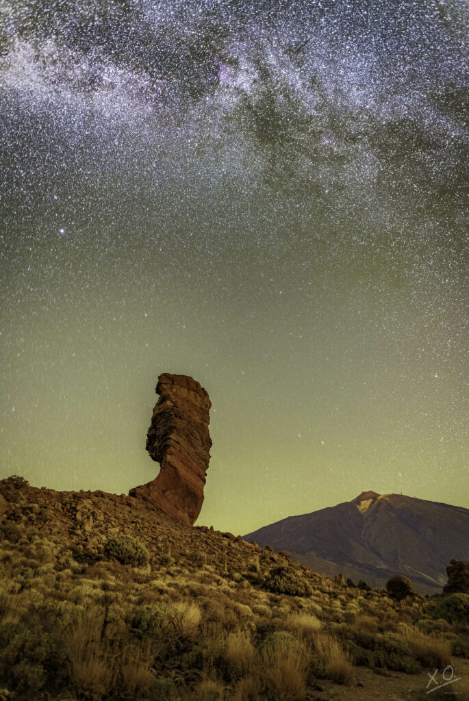 Striking rock formation under starry night sky with rugged terrain and distant mountain landscape Wallpaper