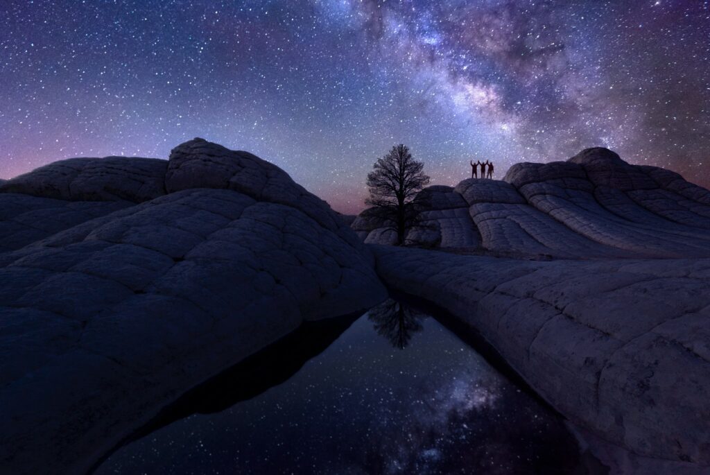 Astrophotography Milky Way over starry sky with rock formations tree reflected in still pool at night Wallpaper