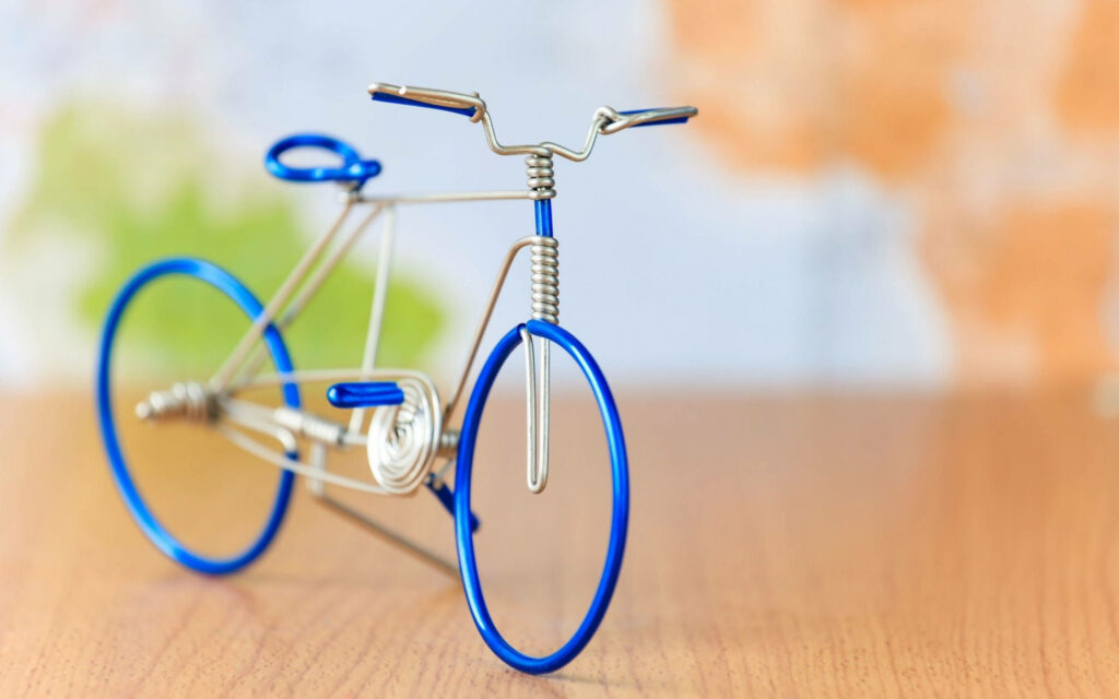Close-up of miniature blue wire bicycle model on wooden surface with blurred colorful background Wallpaper