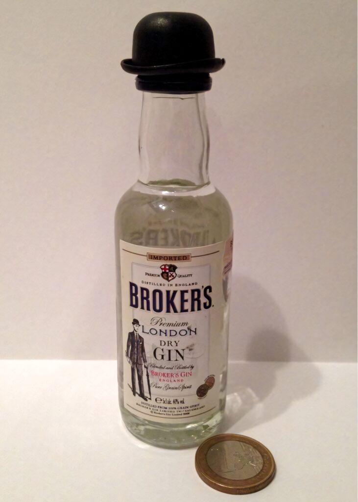 Miniature Brokers Premium London Dry Gin bottle with bowler hat cap beside coin on minimalist background Wallpaper