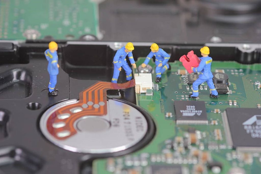 Miniature workers repairing open computer hard drive circuit board detailed tech macro wallpaper