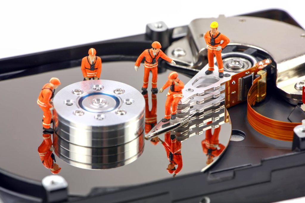 Miniature workers in orange gear repairing open hard disk drive on reflective metallic platter Wallpaper