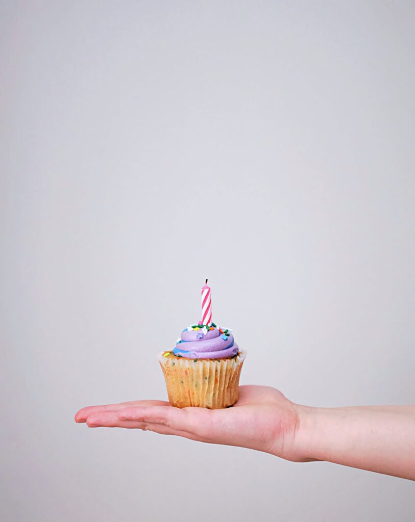 Hand holding cupcake with lavender frosting colorful sprinkles lit pink candle on gray background Wallpaper