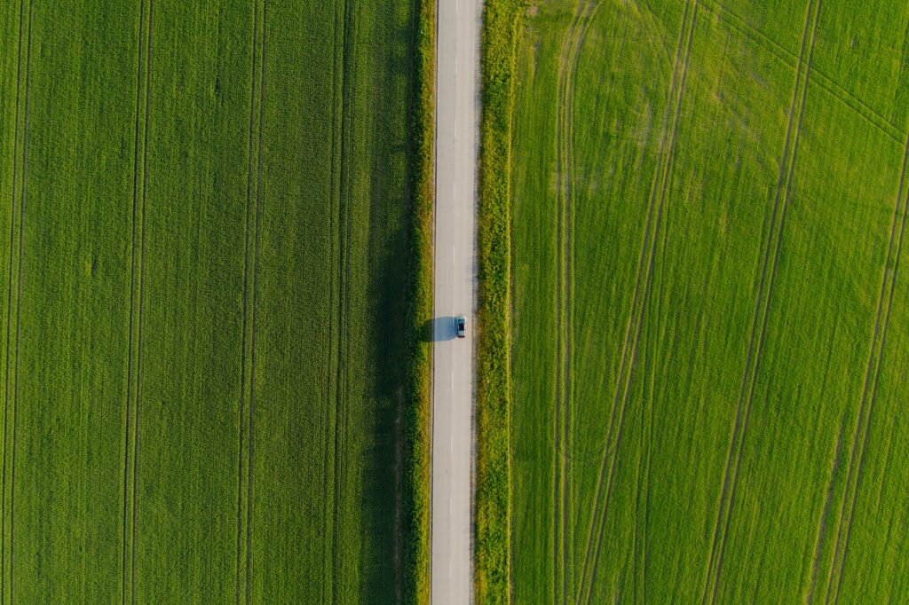 Aerial view of a lone car on a straight road through vibrant green grass fields minimalist wallpaper