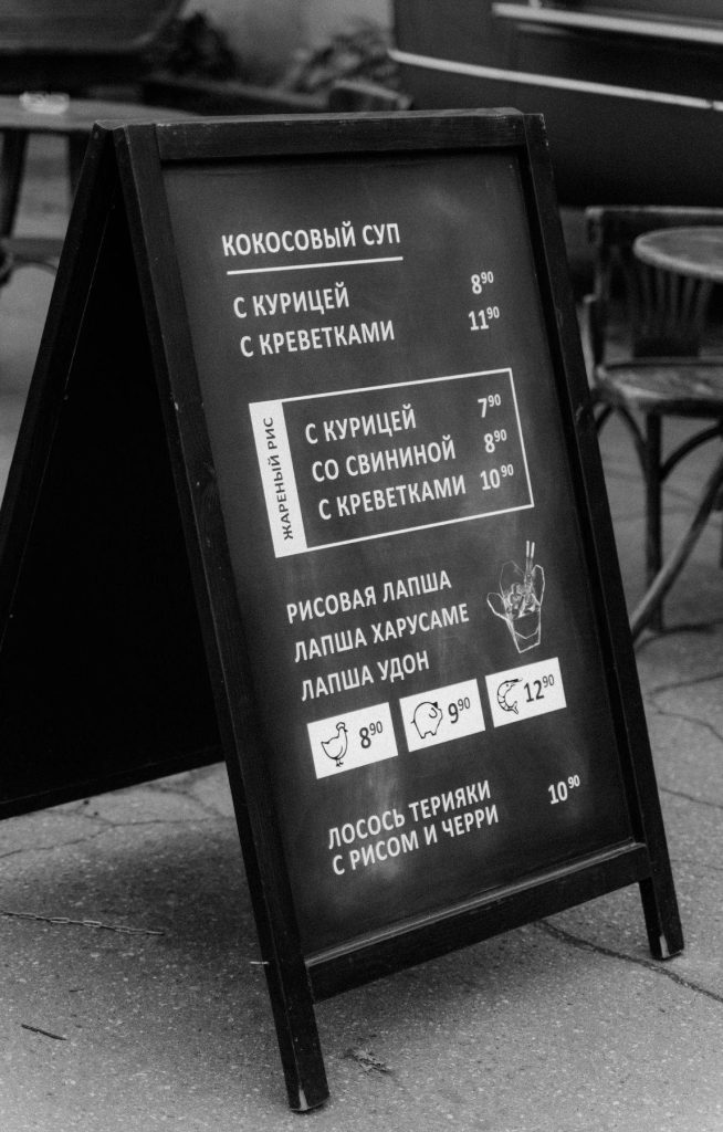 Black and white A-frame sidewalk menu board with Russian Asian dishes in urban cafe setting Wallpaper