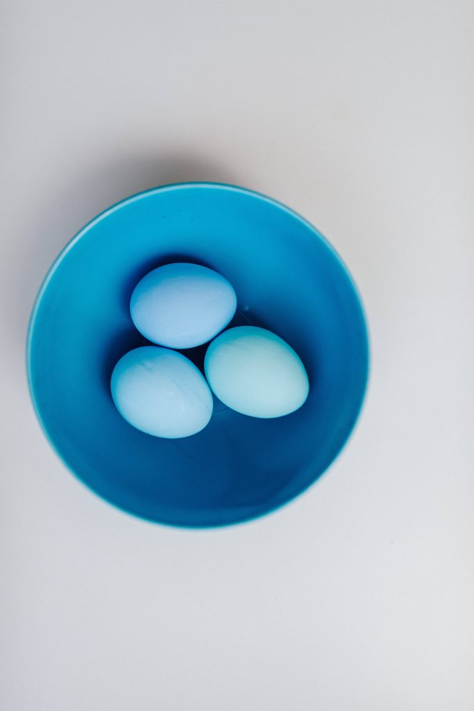 Minimalist Easter wallpaper with three smooth light blue eggs in vibrant blue bowl top view
