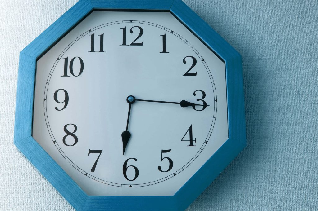 Minimalist blue octagonal wall clock with black numerals on textured matching blue wall background Wallpaper