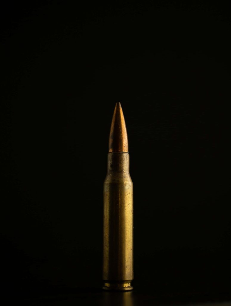 Minimalist brass rifle cartridge standing upright on black background high contrast ammo wallpaper