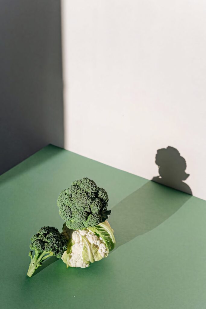 Minimalist wallpaper with fresh broccoli and cauliflower on green surface with natural light shadows
