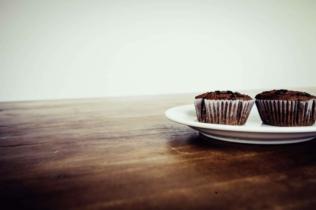 Minimalist wallpaper with two chocolate cupcakes on white plate rustic wooden table background