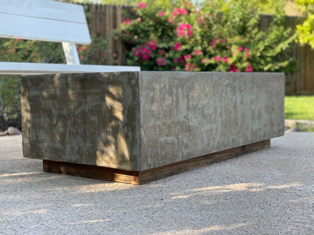 Minimalist concrete table with textured grey top on wooden base in lush outdoor setting Wallpaper
