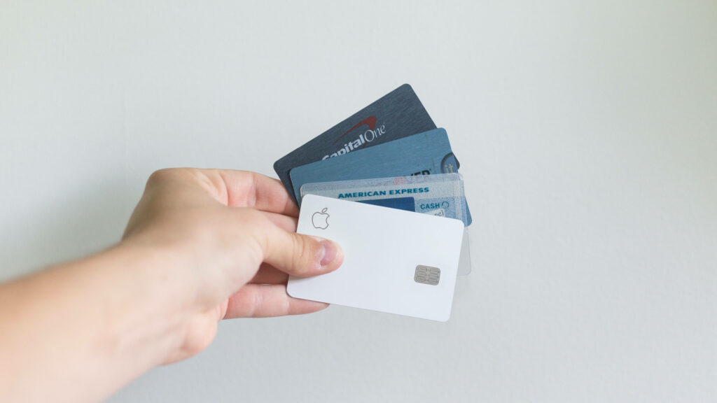 Hand holding fan of credit cards including Capital One American Express and Apple Card on white background Wallpaper
