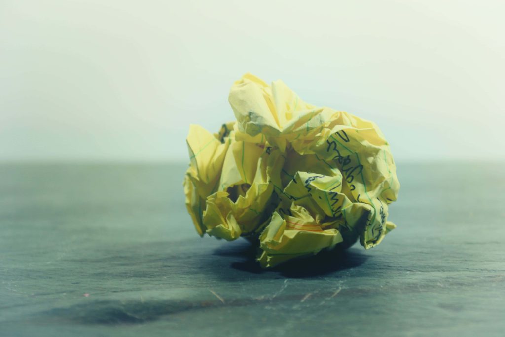 Crumpled yellow lined paper ball on dark slate surface with soft moody lighting wallpaper