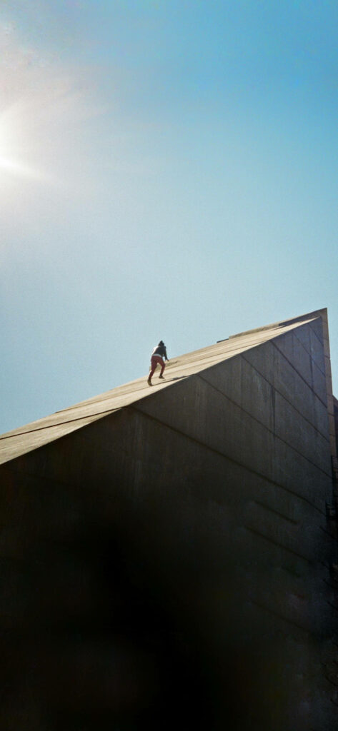 Minimalist Daniel Caesar wallpaper with figure climbing concrete slope under clear blue sky sunlight