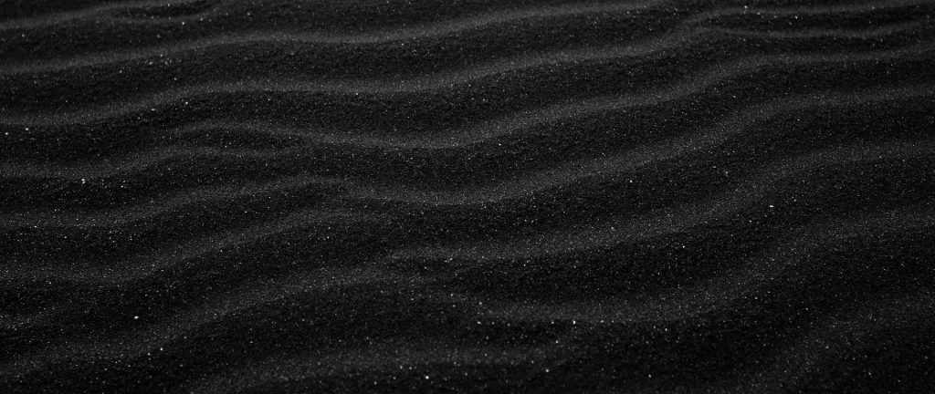 Dark beach sand with detailed ripples textured charcoal grains minimalist wallpaper background