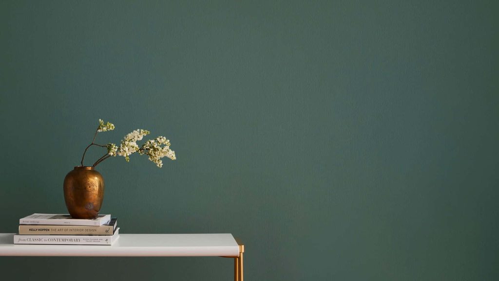 Minimalist workspace with dark green wall white table brass vase and interior design books background Wallpaper