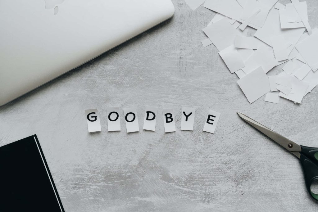 Top-down flat lay of goodbye text with paper letters scissors and scraps on gray desk background Wallpaper